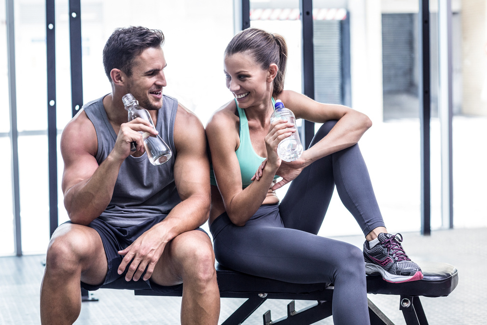 Muscular couple discussing on the bench and holding water bottle